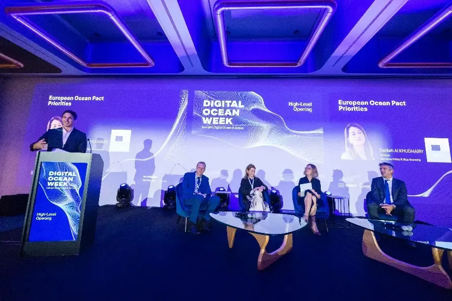 A speaker at a lectern and four seated panellists on a stage beneath a 'Digital Ocean Week' screen.