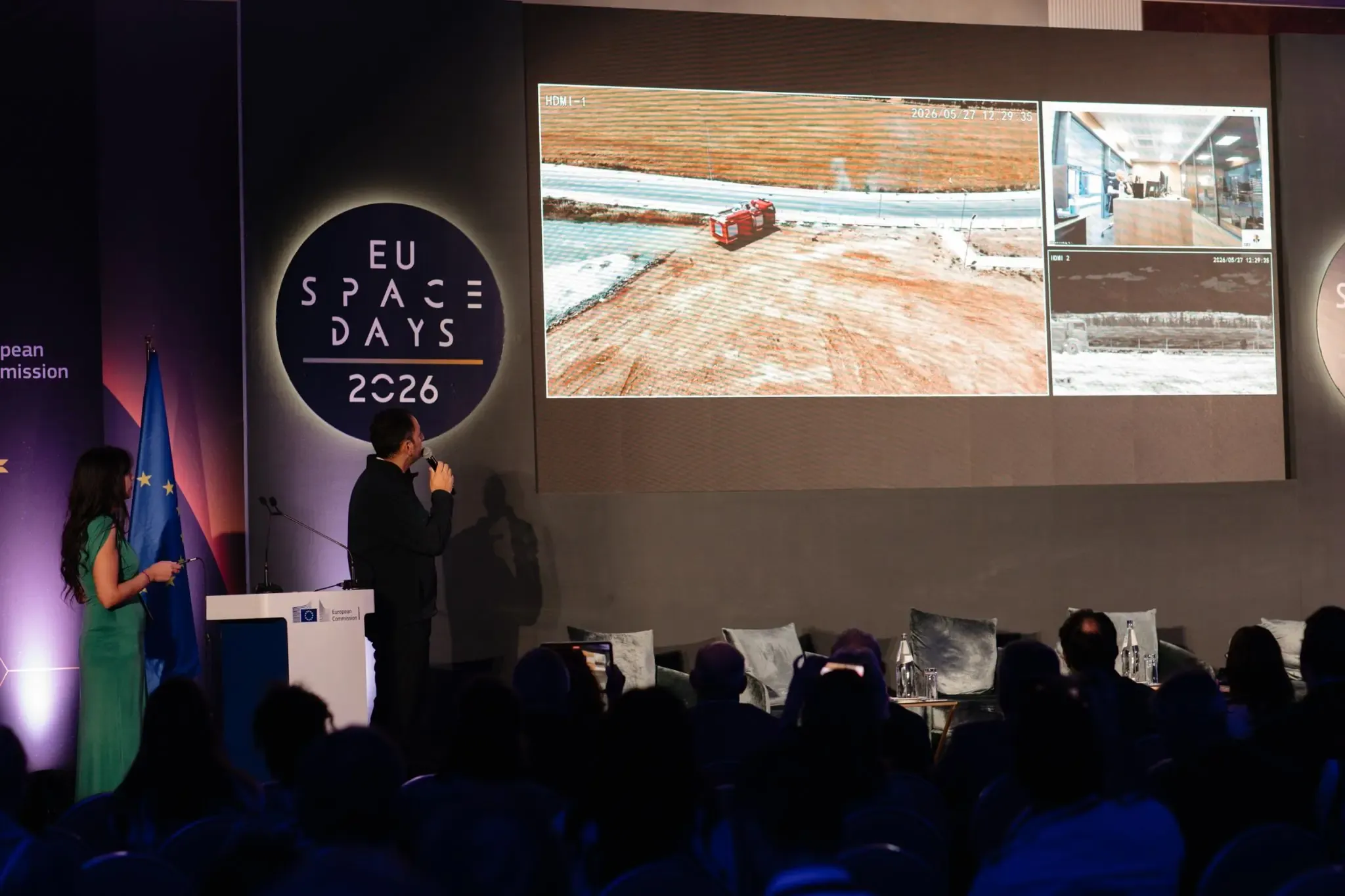 Two presenters on stage at EU Space Days 2026 demonstrate a GOVSATCOM live video feed showing a wildfire response scenario, with field equipment imagery displayed on a large screen to illustrate satellite-supported situational awareness.