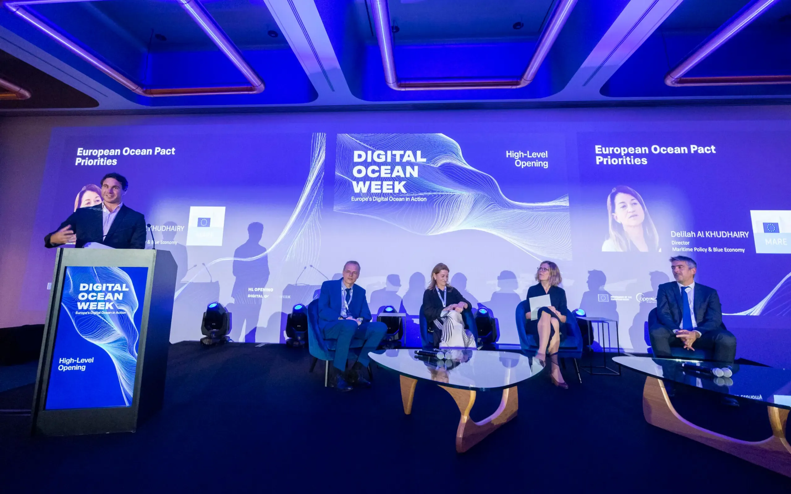 A speaker at a lectern and four seated panellists on a stage beneath a 'Digital Ocean Week' screen.