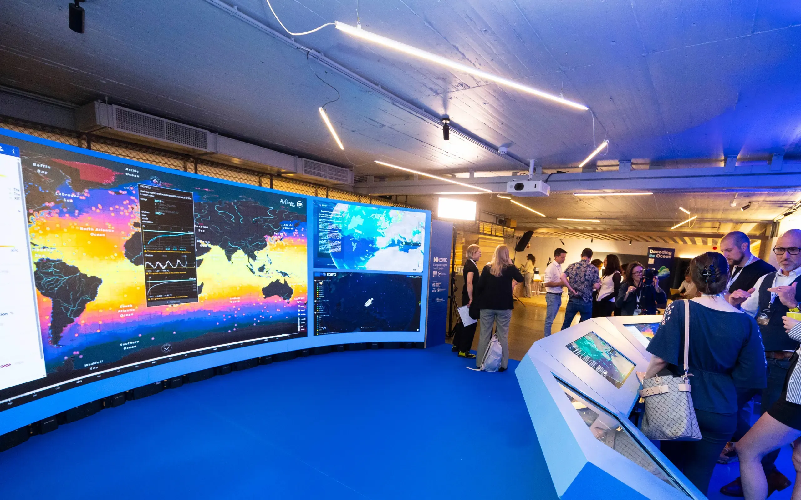 A large curved display screen showing ocean monitoring dashboards, including a colour-coded sea surface temperature globe on the left and European Digital Twin Ocean visualisations on the right.