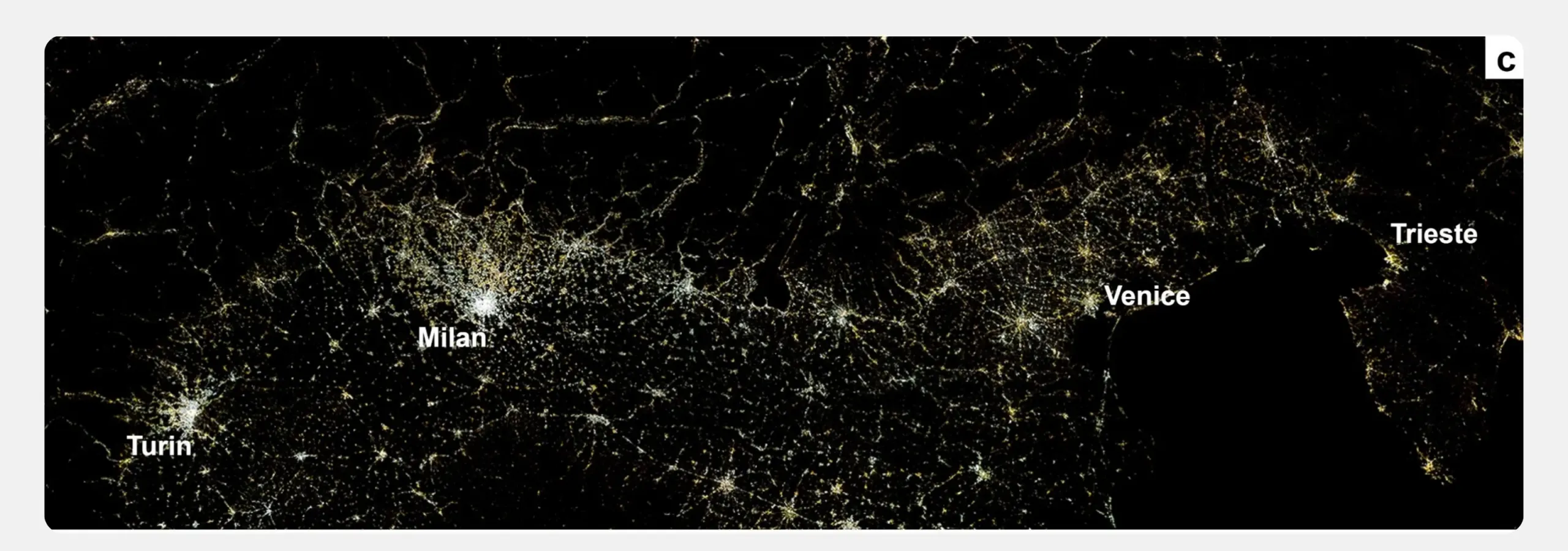 A nighttime satellite view of Northern Italy, showing cities as bright clusters of light linked by a dense network of smaller lights. Milan is the largest cluster near the centre, with Turin, Venice, and Trieste also labelled; the dark Adriatic Sea sits at the right.