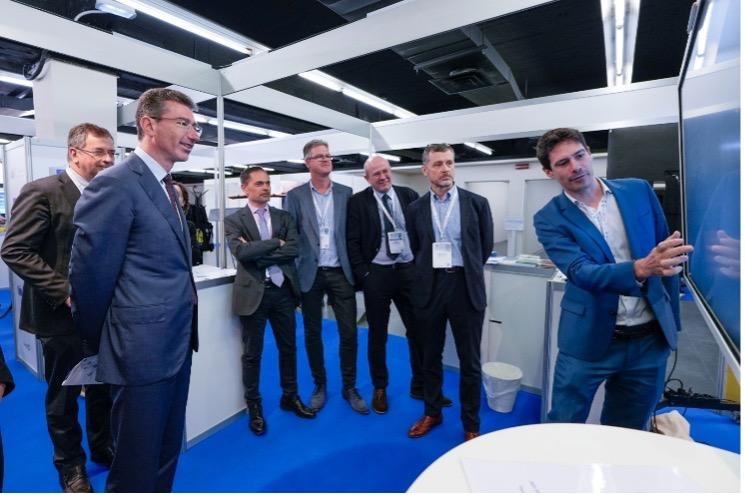 A group of professionals gathered around a presentation screen in a modern exhibition space, engaged in discussion and analysis.