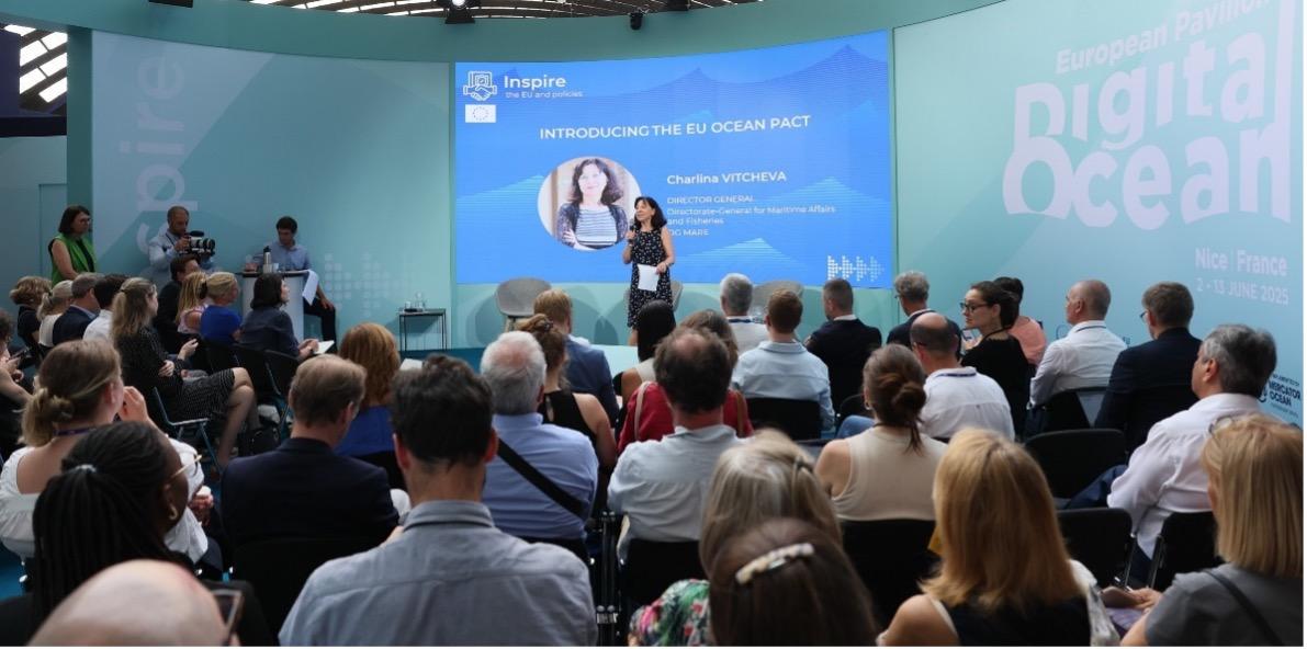 A diverse audience gathers at a conference in Nice, France, focused on the EU Ocean Pact, with a speaker addressing them on stage.