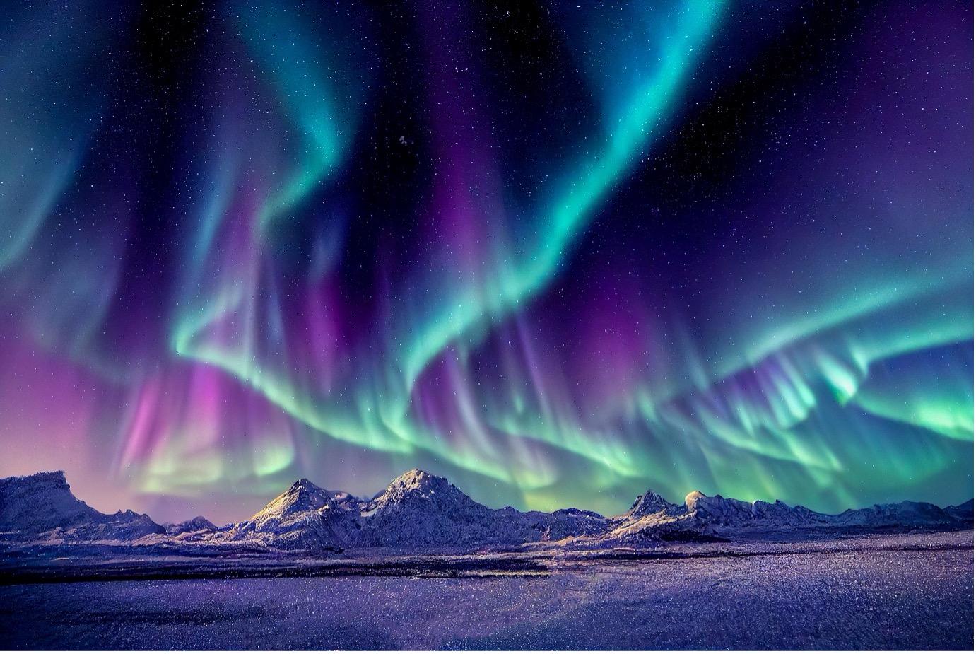 The aurora borealis illuminates the night sky above mountains, showcasing vibrant colors from solar activity.