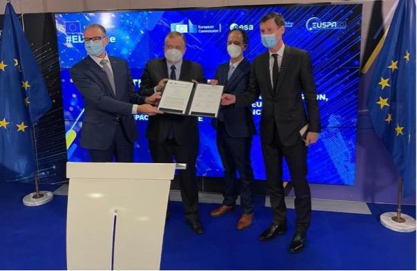 Four men in suits and face masks pose for a photo, holding a signed document. The backdrop features the #EUSpace hashtag along with logos from the European Union, ESA, and EUSPA.