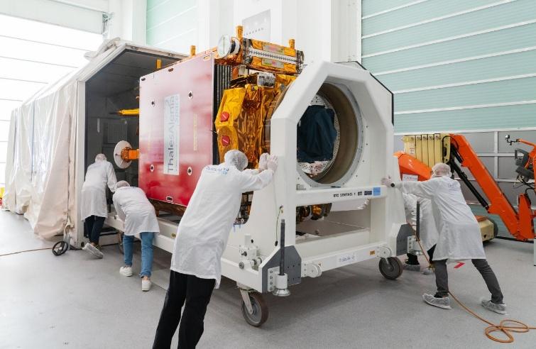 Engineers in cleanroom suits are maneuvering the Copernicus Sentinel-1 satellite on a transport platform inside a cleanroom facility. The satellite is partially wrapped in thermal insulation with visible gold and red panels, and it is being moved towar...