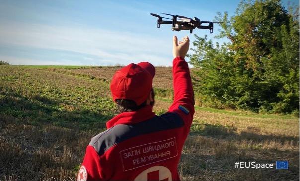 A man in a red shirt proudly holds a small drone, showcasing his interest in technology and aerial devices.